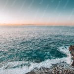 Blue Sea and Sky Orange Horizon Ship Rocky Cliff background image & Google Slides Theme